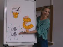A woman explaining a cardboard on wich it is written "win win" @ Sequel Prod / RTBF / Proximus
